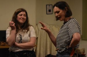 Two female actors stand in conversation