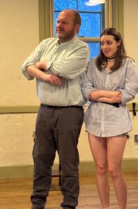 Amana and a woman standing with arms folded, looking on in slight amusement