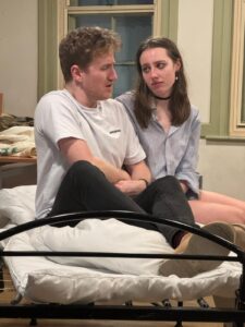 Man and a woman sitting on an unmade bed, talking