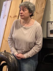 A woman stands in a bemused pose, next to a tuba
