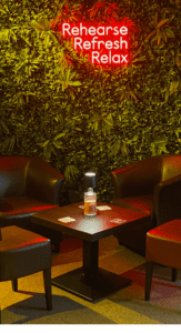 Image of the members's bar, with its green plant wall and neon sign containing the words "Rehearse, Refresh, Relax"