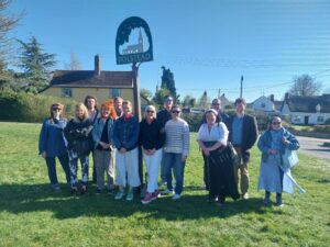 Cast and crew of The Ballad of Maria Marten beside the village sign in Polstead Suffolk