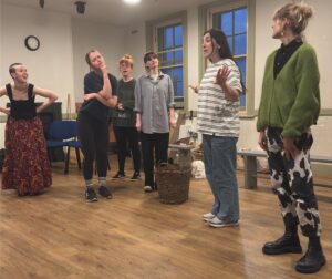 Group of standing female actors, one leading a song