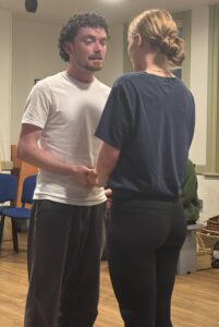 Male and female actor stand holding hands and looking into each other's eyes in a tender scene