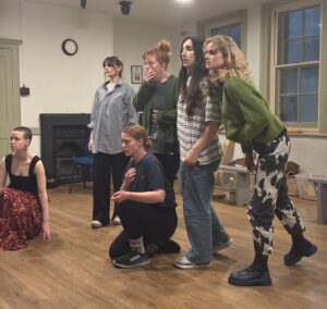 Six female actors look in same direction in a state of shock at something they can see in the distance