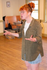 A female actor speaks animatedly, hands outstretched