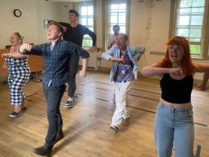 Three male and three female actors promenade forward in a dance, singing as they go