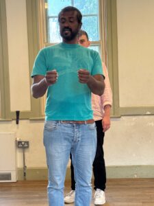A man stands holding an imaginary map, with another behind him