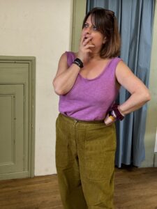 A woman stands with hand to mouth in a puzzled pose, hand on hip