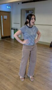 A woman stands singing, hands on hips