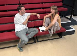 Male and female actor sit chatting on a bench in a relaxed manner