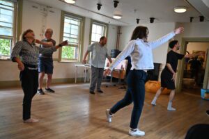 Two female and three male actors stand with arms outstretched as though dancing