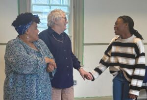 An older actor holds the hand of a younger, who is smiling, while another actor looks on