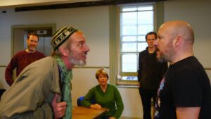 Two men stand facing each other in conflict, with others looking on behind them