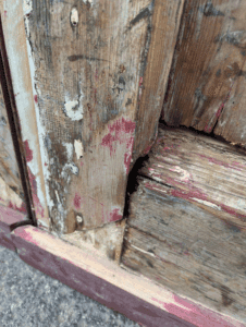 A close up of the bottom of a wooden door showing gaps between old joins in the woodwork.