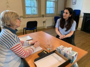 Two female actors in conversation sit across a desk from each other