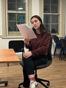A female actor sits on an office chair reading a contract