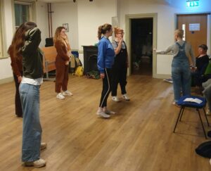 Five female actors stand receiving instructions on movement