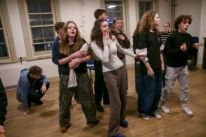 Several young actors in a variety of agitate poses, all looking in one direction