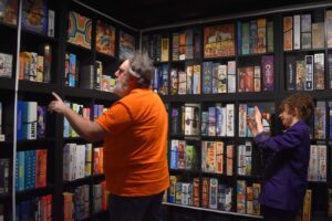 A man in an orange T-shirt stands searching through a shelf of games