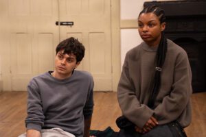 A young man and woman sit on the floor, listening to someone speaking off camera