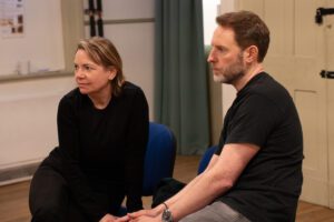 A man and a woman sit facing and listening to someone off camera