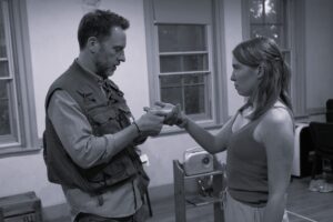 A male actor holds and examines the hand of a female actor standing opposite him