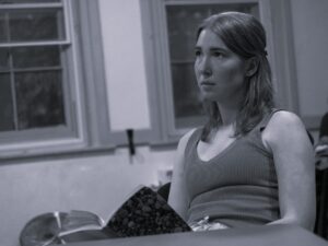 A female actor sits with a n open book in her hand, looking into the distance