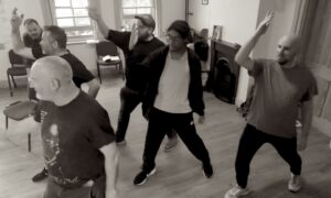 Five male actors strike a pose in a dance move, arms in the air