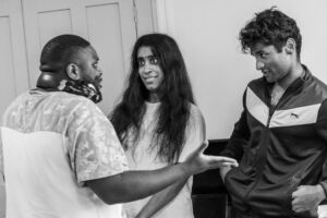 Two male and one female actor stand in conversation