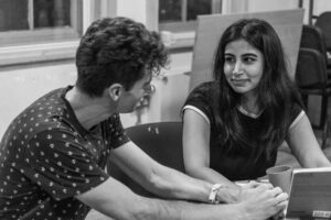 A male and a female actor sit at a table in close conversation
