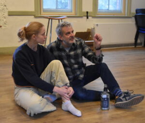 A female actor and an older male actor telling a story sit together on the floor,